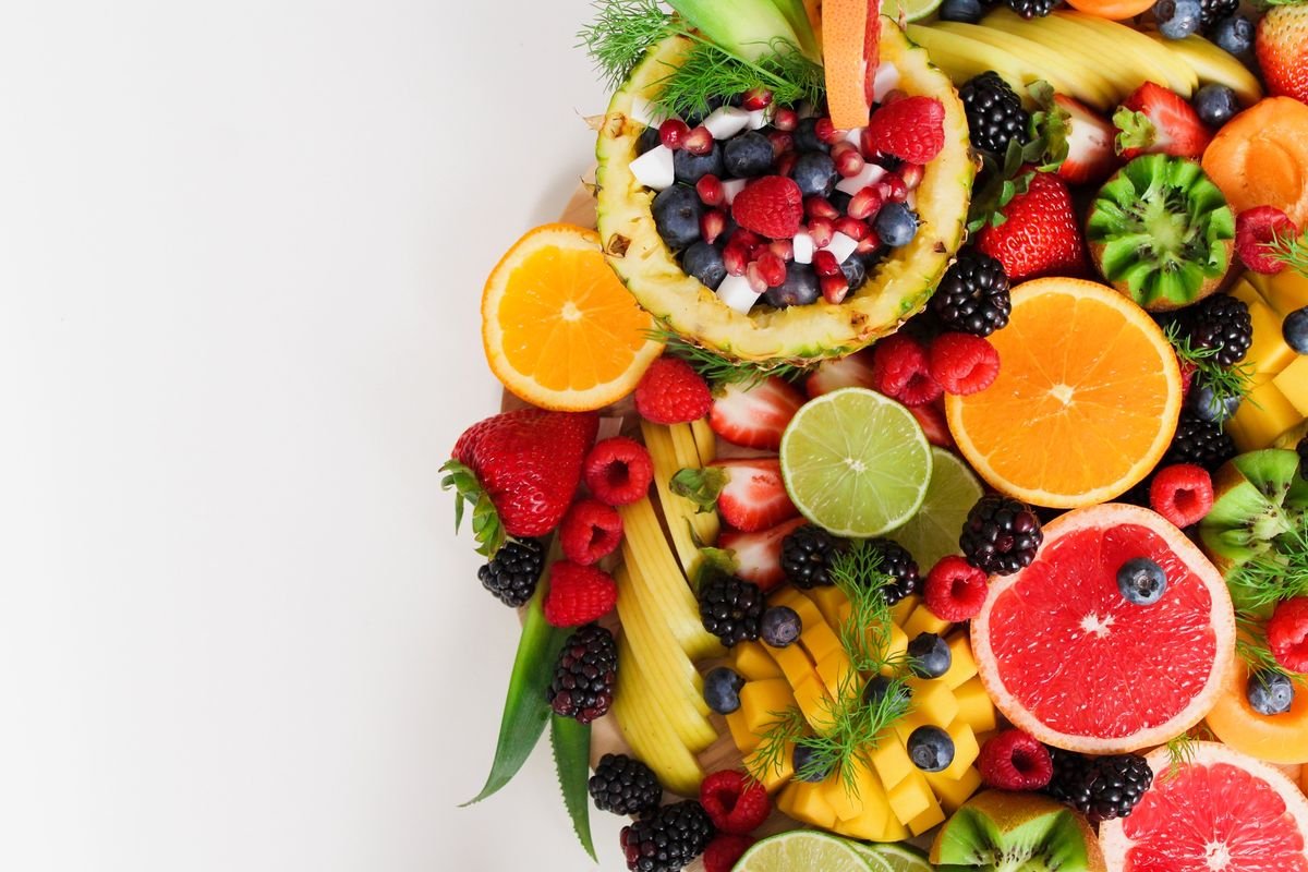 Flat lay of a halved pineapple filled with berries, surrounded by orange, lime, grapefruit, strawberries, kiwi and blackberries on white